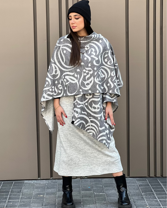 Woman wearing a patterned poncho and skirt against a beige wall.